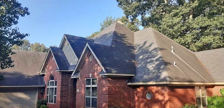 Before: Brick home with streaked gray shingles after roof stain removal in central Arkansas